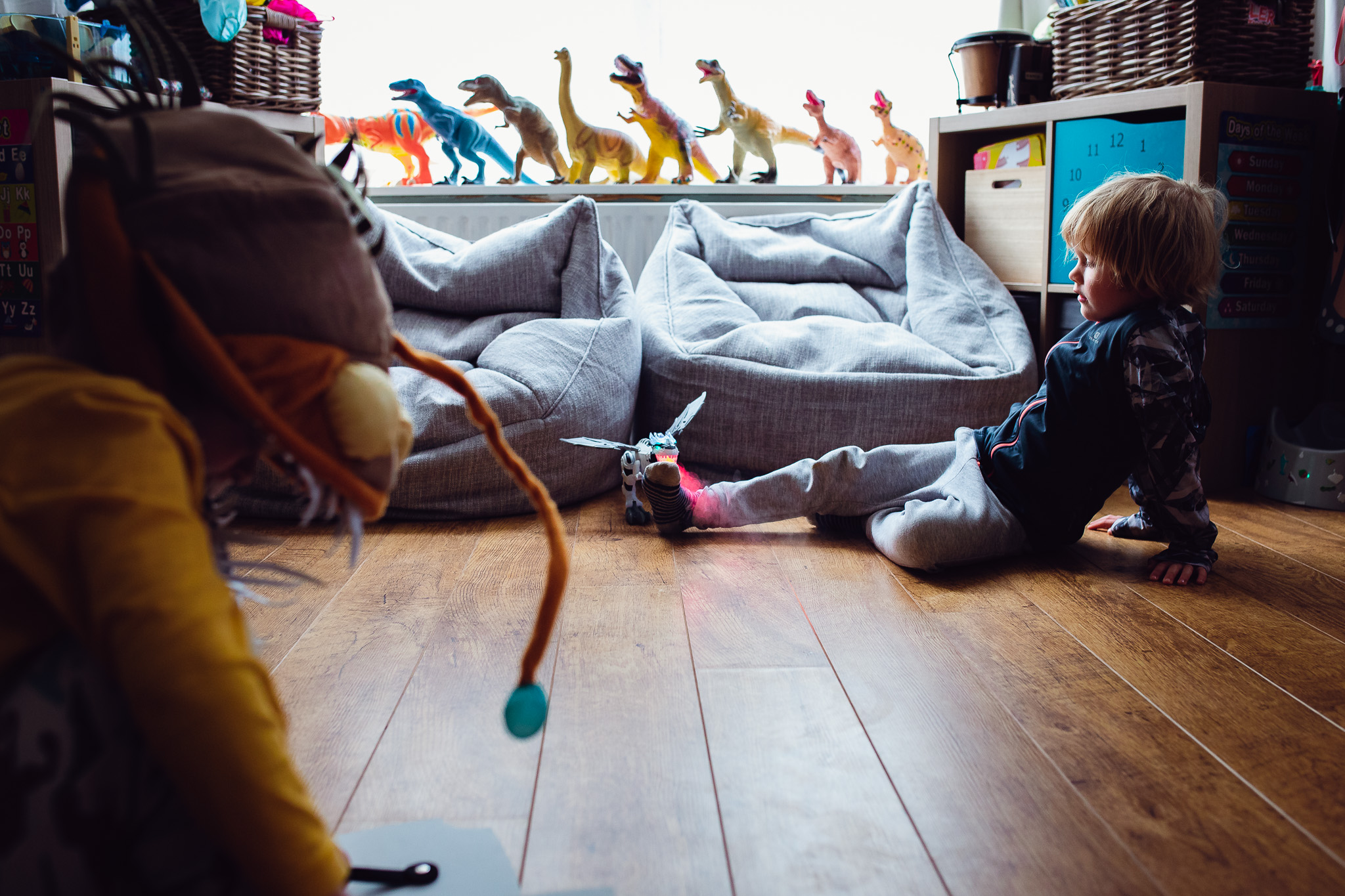 Leo and Kai are playing in their game room with dinosaurs on a windowsill during a family photo session.