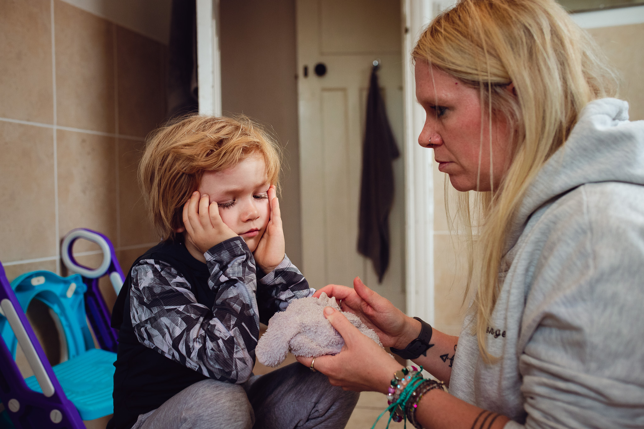 Kai looks sad after a fall sitting with his mum in the bathroom during a family photo session.