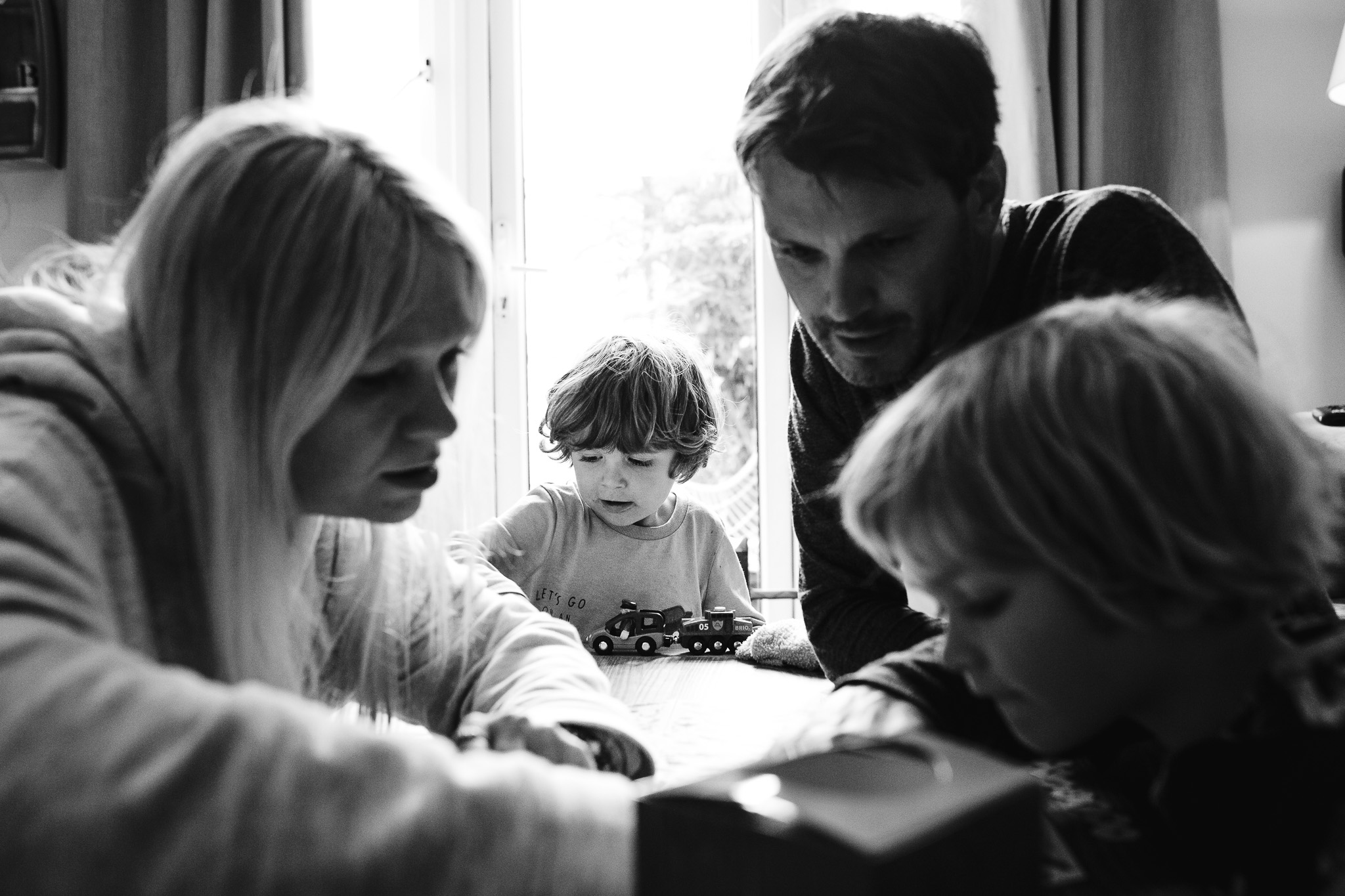 Dad, mum and Kai look at something together whilst Leo plays with toys during a family photo session.