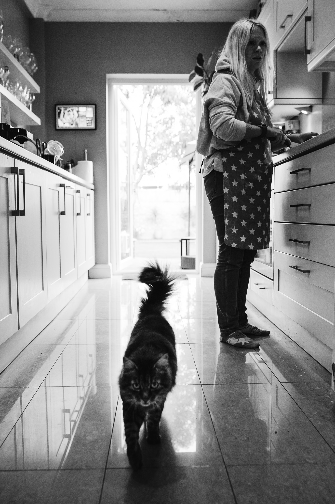 Mum is preparing food in a galley kitchen with a cat walking through during a family photo session.
