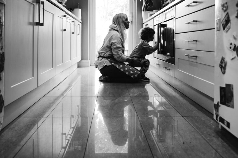 Mum and son sitting together on the kitchen floor in front of an oven watching during a family photo session