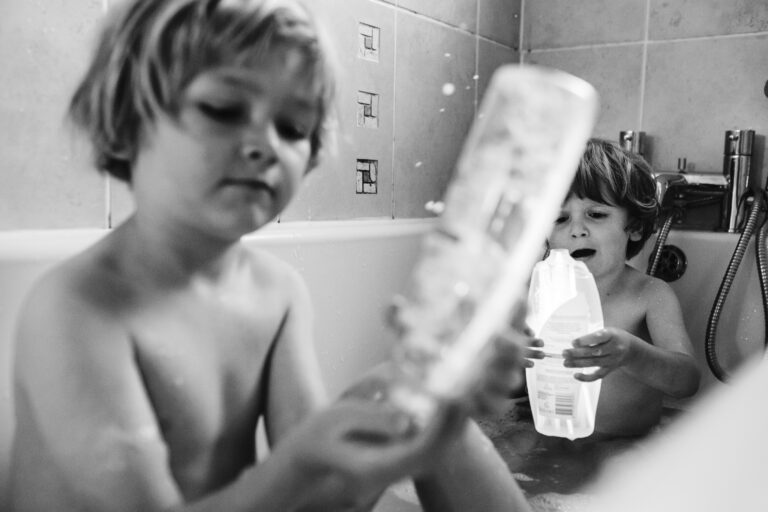Two young boys playing with bottles and glow sticks in a bath during a family photo session.