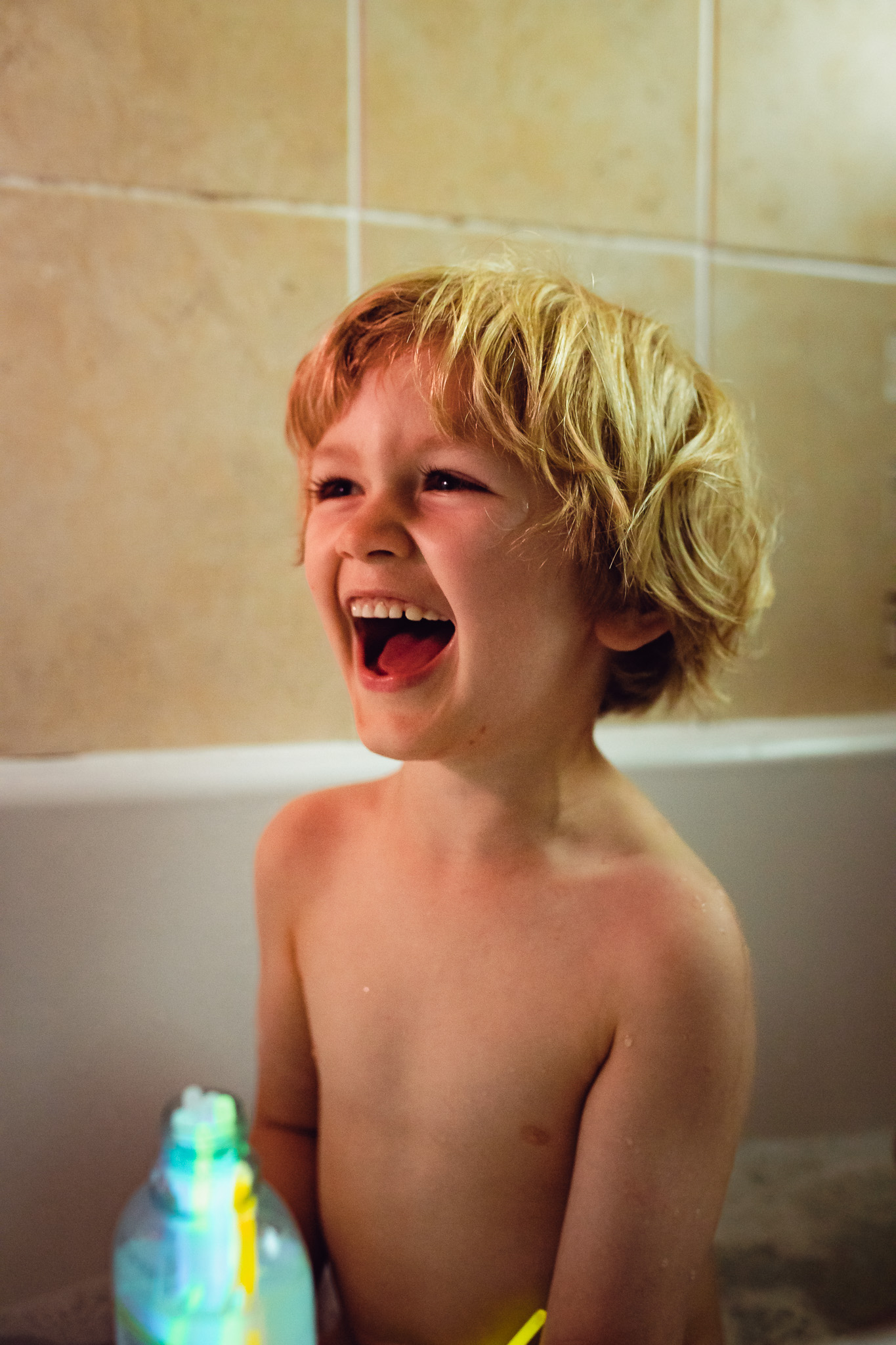 Kai laughing in a bath whilst holding a bottle filled with glow sticks during a family photo session.