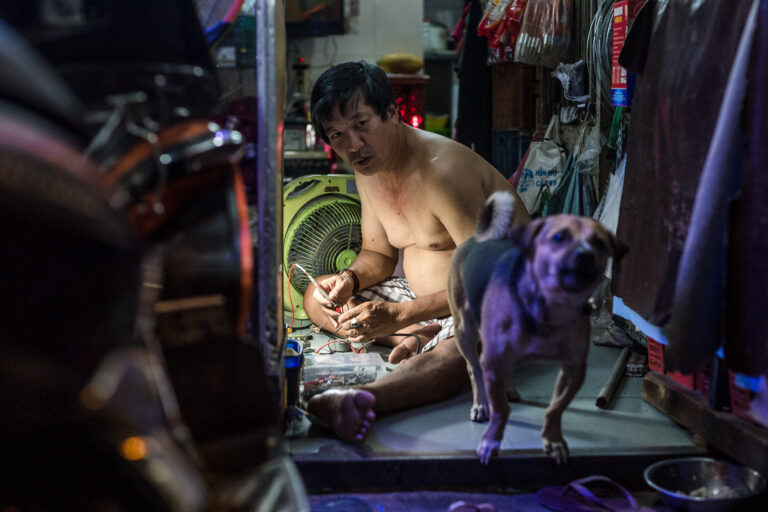 Vietnamese mechanic captured in a candid portrait sitting on a floor with a little barking dog