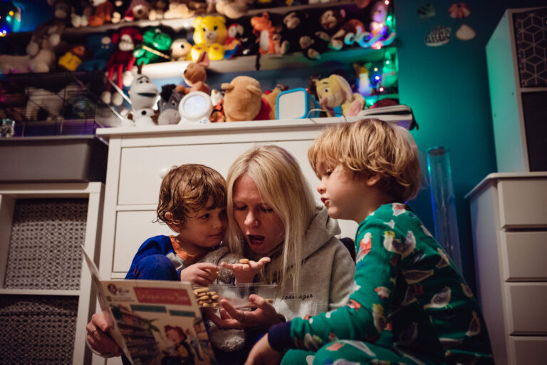 Mum reading bedtime stories with two sons and eating biscuits in their bedroom during a family photo session.