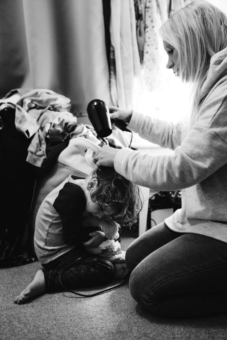 Mum is drying her son's hair while he cuddles his teddy during a family photo session.