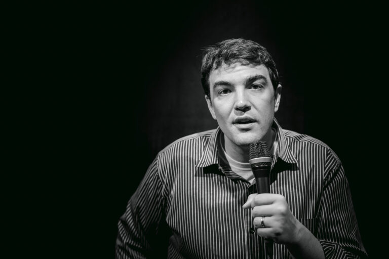 A young male comedian holding a microphone up to his face posing for a portrait