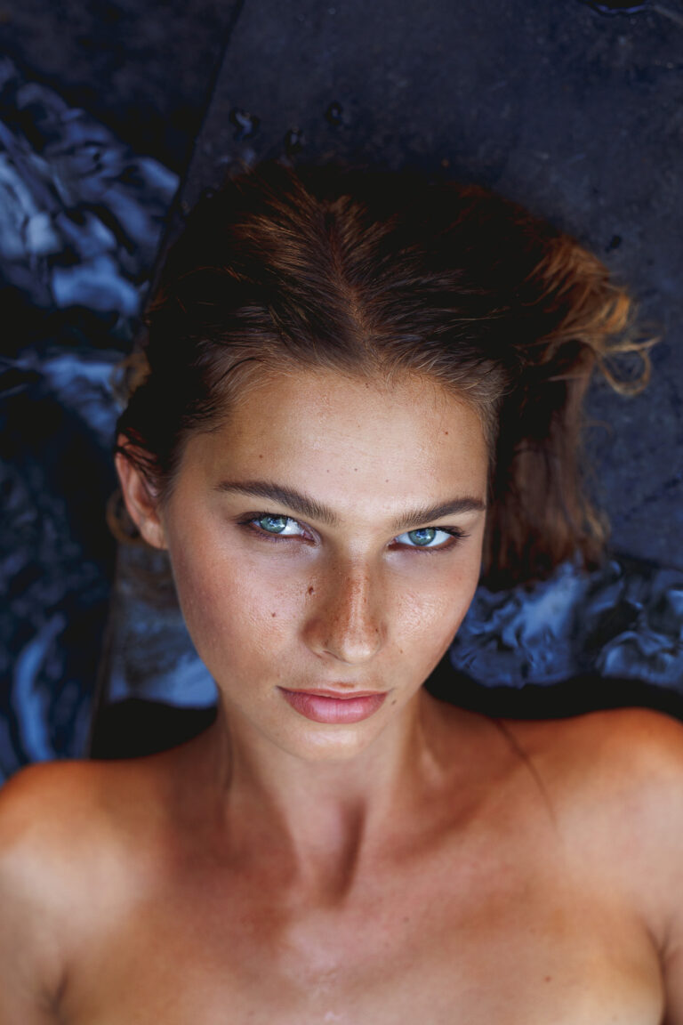 A young woman poses for a fashion portrait whilst lying down next to a pool