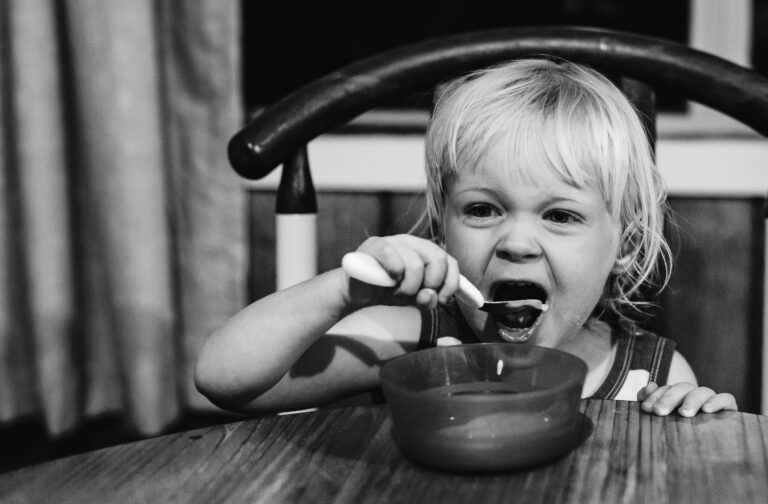 A toddler with mouth wide open eating yoghurt with a spoon