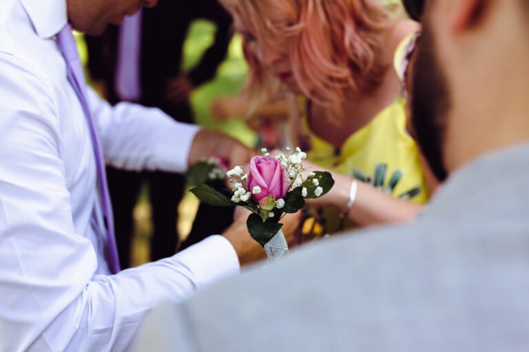 Pink rose buttonhole with people getting ready for a wedding in the background.