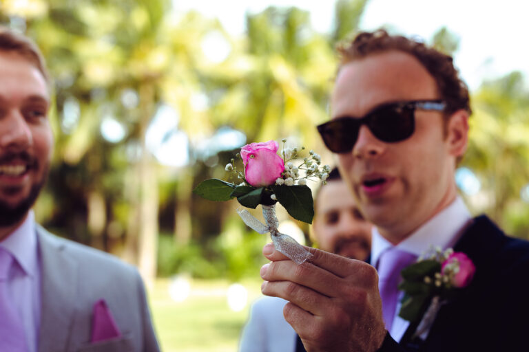 A groomsman holding up a pink rose buttonhole.
