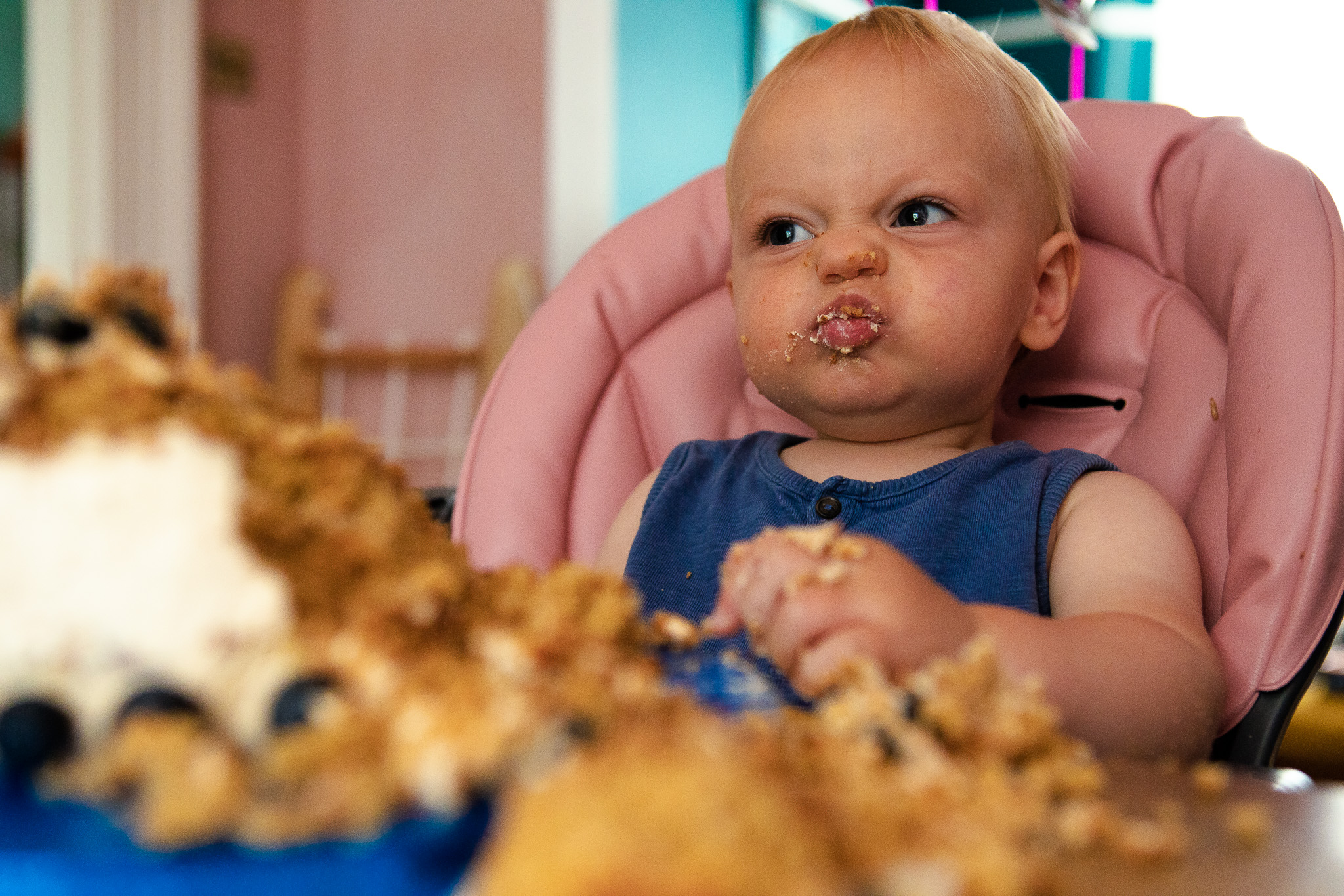 portrait of a baby during a cake smash scrunching up its face and eating a blueberry cake