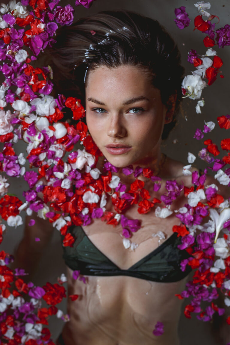 A young woman poses for a fashion portrait in a bath full of petals wearing a thaikila bikini