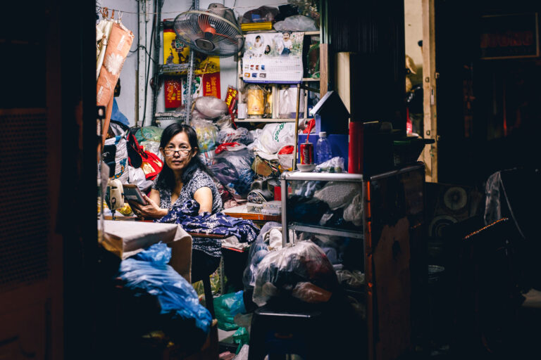 A candid portrait of a Vietnamese woman sitting in her sewing stall at night