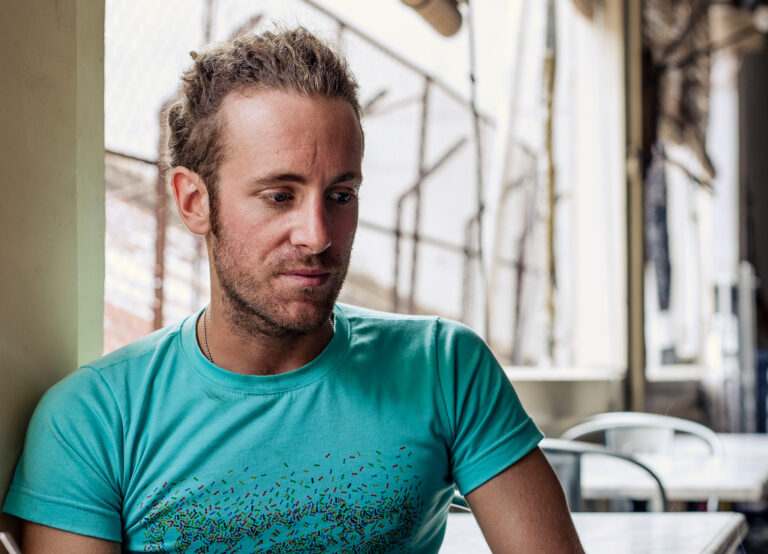 a young man wearing a turquoise t-shirt poses for a portrait for Word Magazine