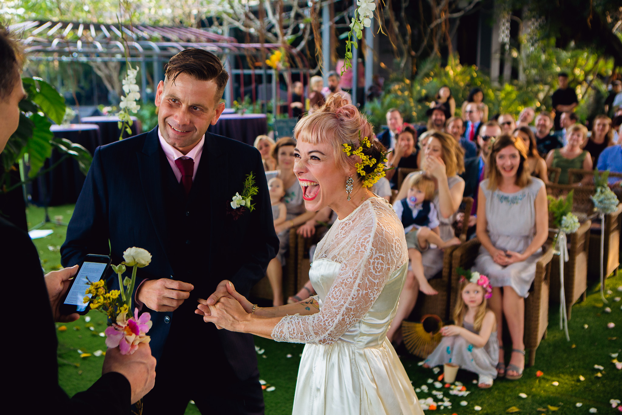 Bride and groom laughing as they get blessed with flowers at wedding ceremony.