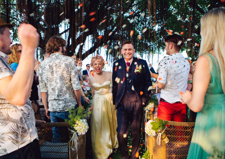 Bride and groom smile and walk down the aisle surrounded by guests and confetti at their destination wedding.