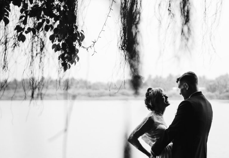 Bride and groom smile and look at each other under a tree canopy during their couple portraits.