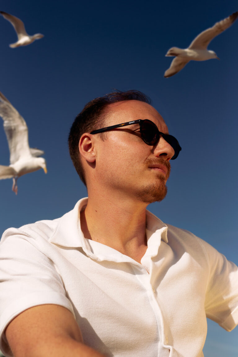 an outdoor headshot of a music producer surrounded by seagulls at Brighton beach