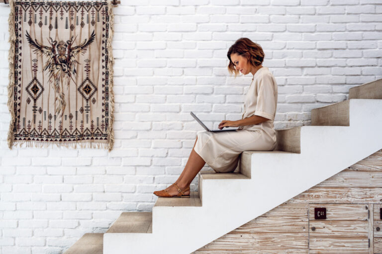 A young professional female poses for a portrait as she sits on stairs with a laptop on her knees