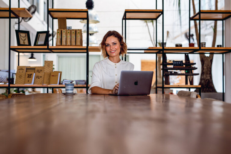 A young female professional sitting with her laptop at a cafe poses for a portrait