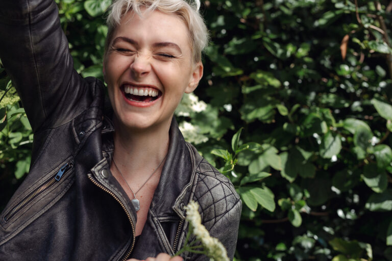 An outdoor headshot of a young woman wearing a jacket laughing
