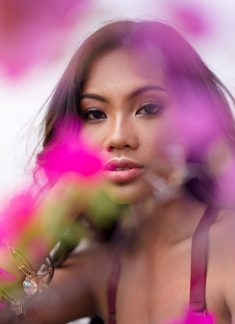 A young woman looking through pink flowers poses for a portrait