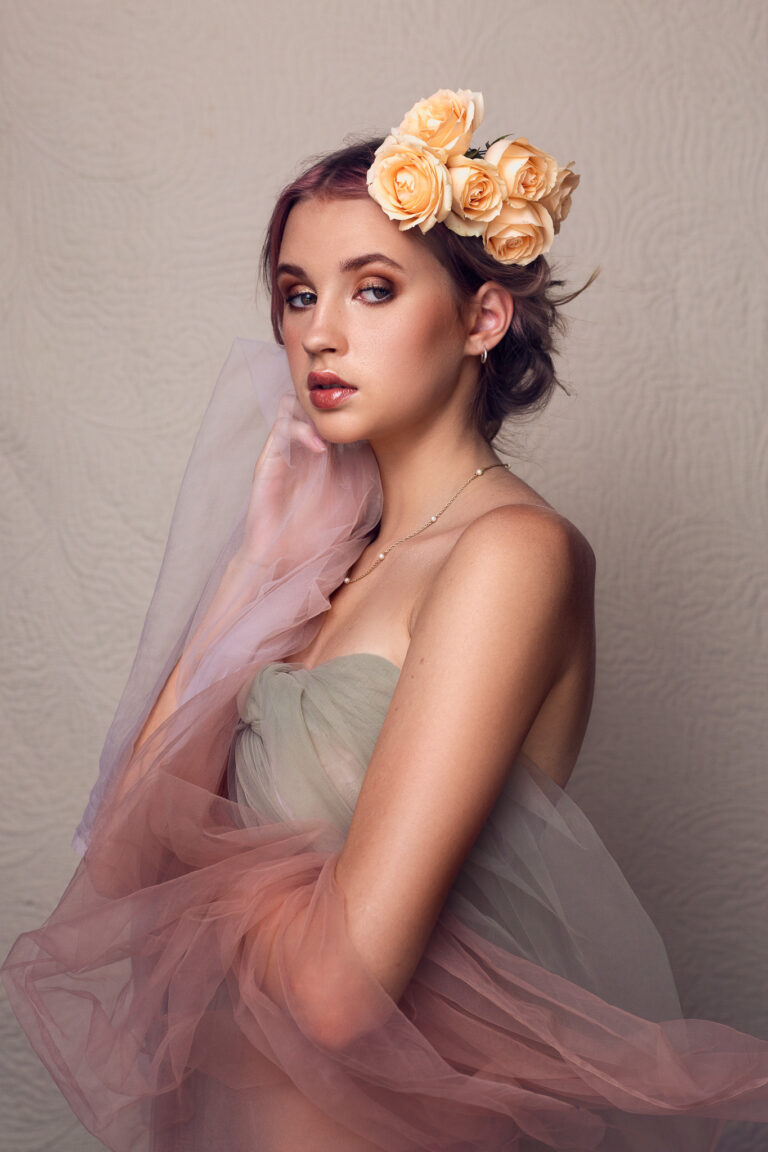 A young woman with peach roses in her hair wearing tulle poses for a portrait in Rozewin Photography studios