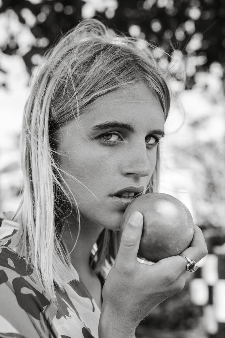 a young woman poses for a portrait holding an apple to her lips