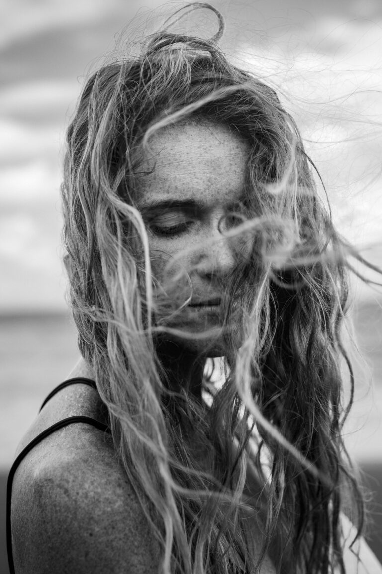 A young freckled woman with wind swept hair closes her eyes during a portrait session