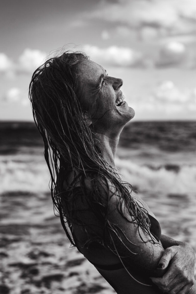 A young woman throws her head back and laughs while posing for a portrait on a beach in Bali