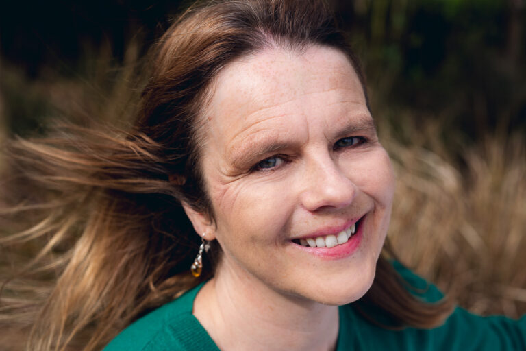 An outdoor headshot of a smiling woman with wind swept hair