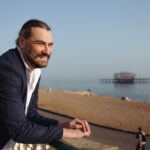 outdoor headshot of a smiling young professional man at Brighton West Pier