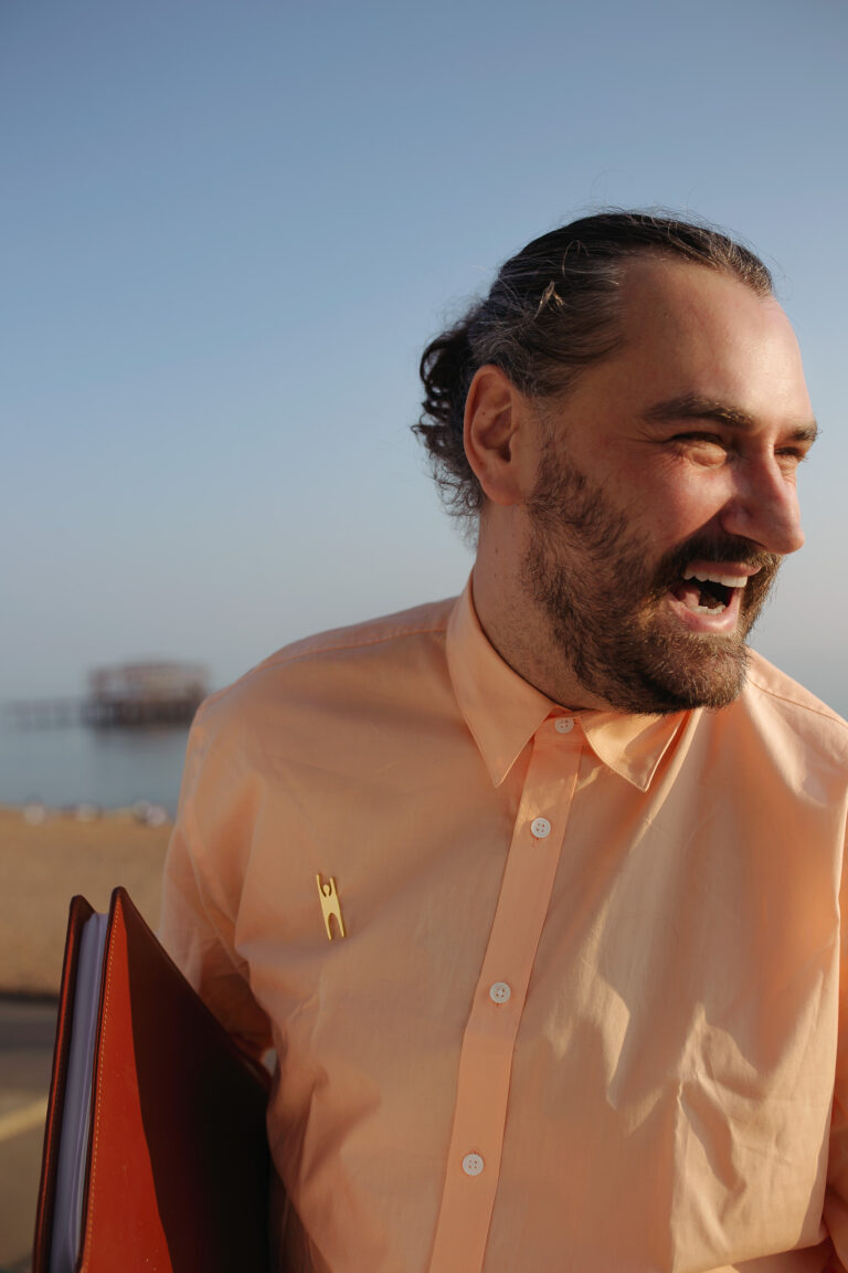 An outdoor headshot of a wedding officiant holding folders and laughing at Brighton West Pier