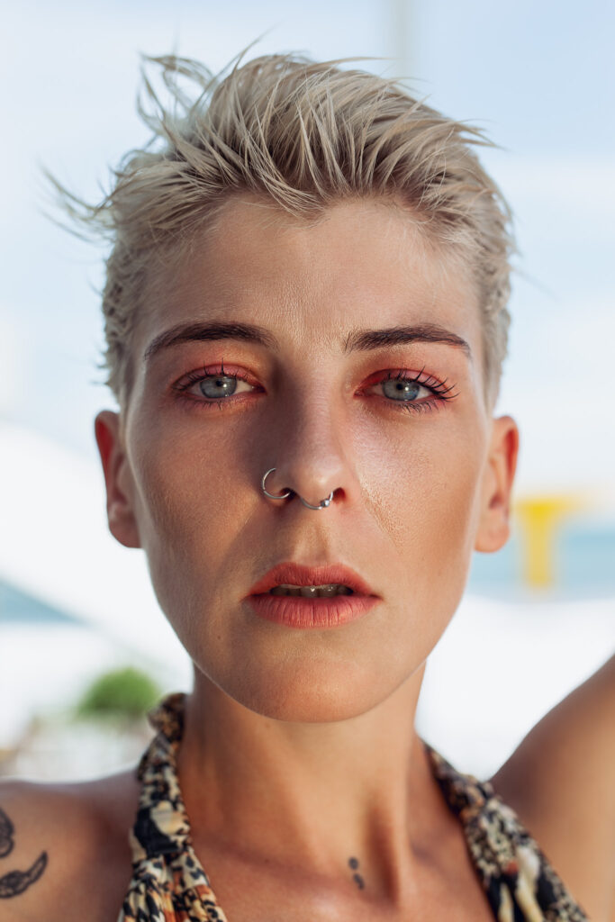 A young woman with short blonde hair and two nose piercings poses for a portrait
