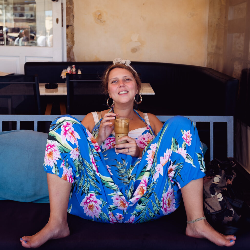 a young woman wearing a dancing leopard jumpsuit sitting with her legs up and drinking coffee