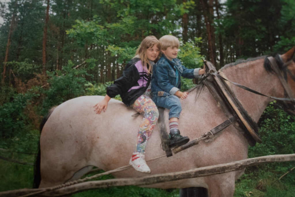 a young boy and girl sitting on a large cart horse in a forest