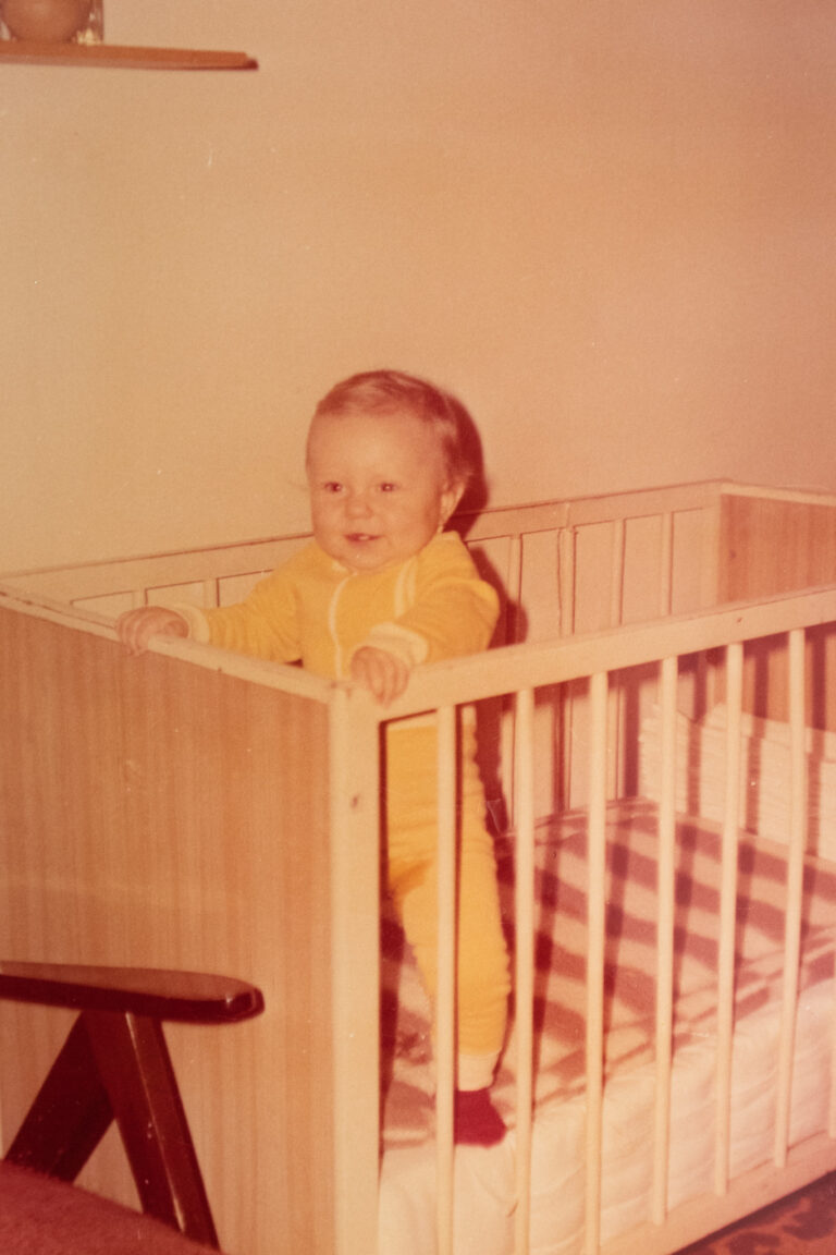 baby standing in a crib wearing a yellow onesie