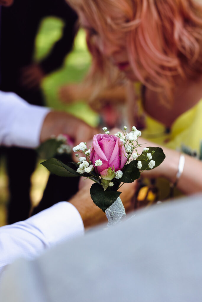 Pink rose buttonhole with people getting ready for a wedding in the background.