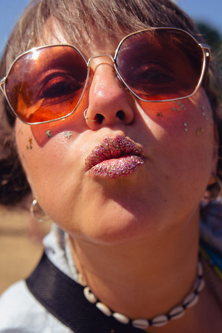 portrait of Olga Rozewin wearing sunglasses with glitter lips at a festival
