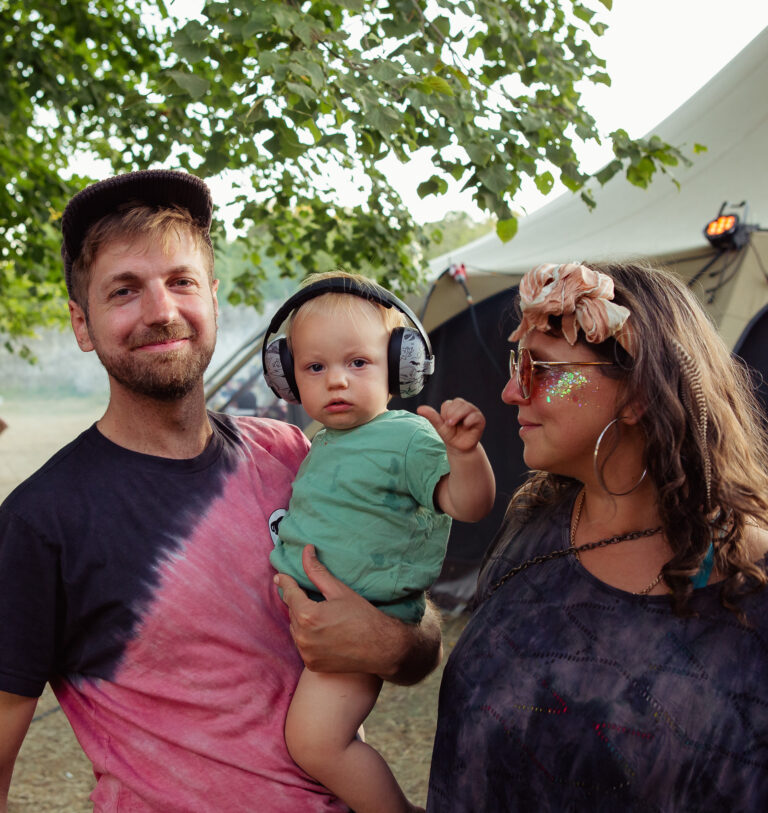 family of a man and woman with glitter on her face and a baby boy wearing protective headphones