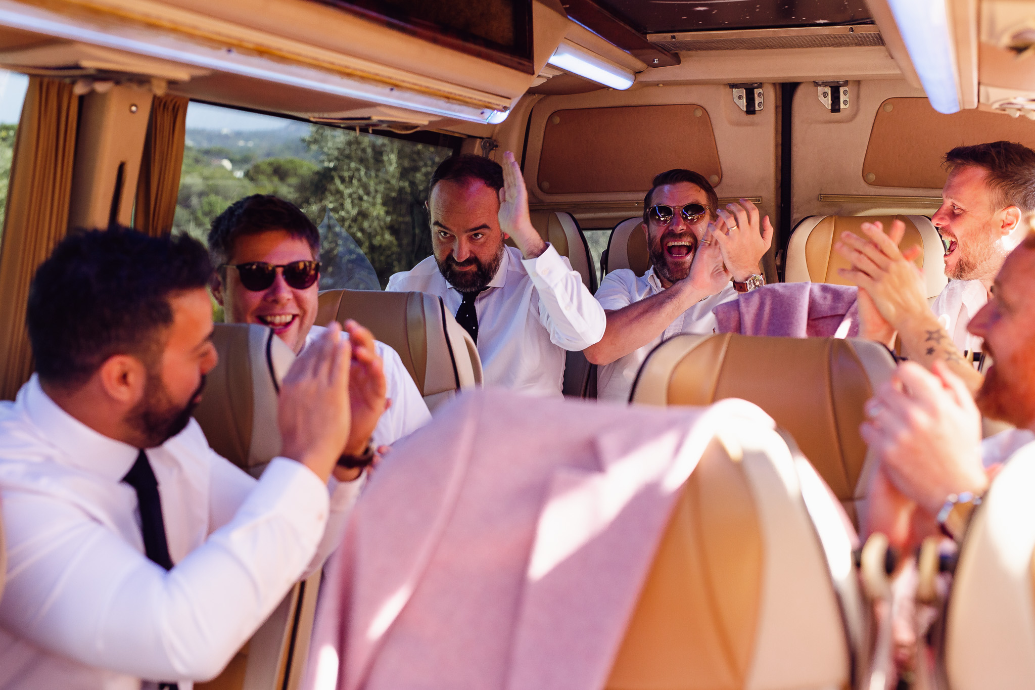 Tom waves as his groomsmen cheer him on whilst they drive to the wedding in a mini bus.