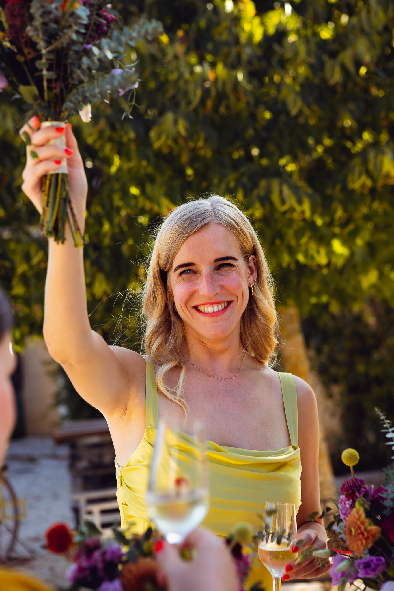 Bridesmaid smiles happily and raises her bouquet at wedding reception in Ambelonas Vineyard, Corfu