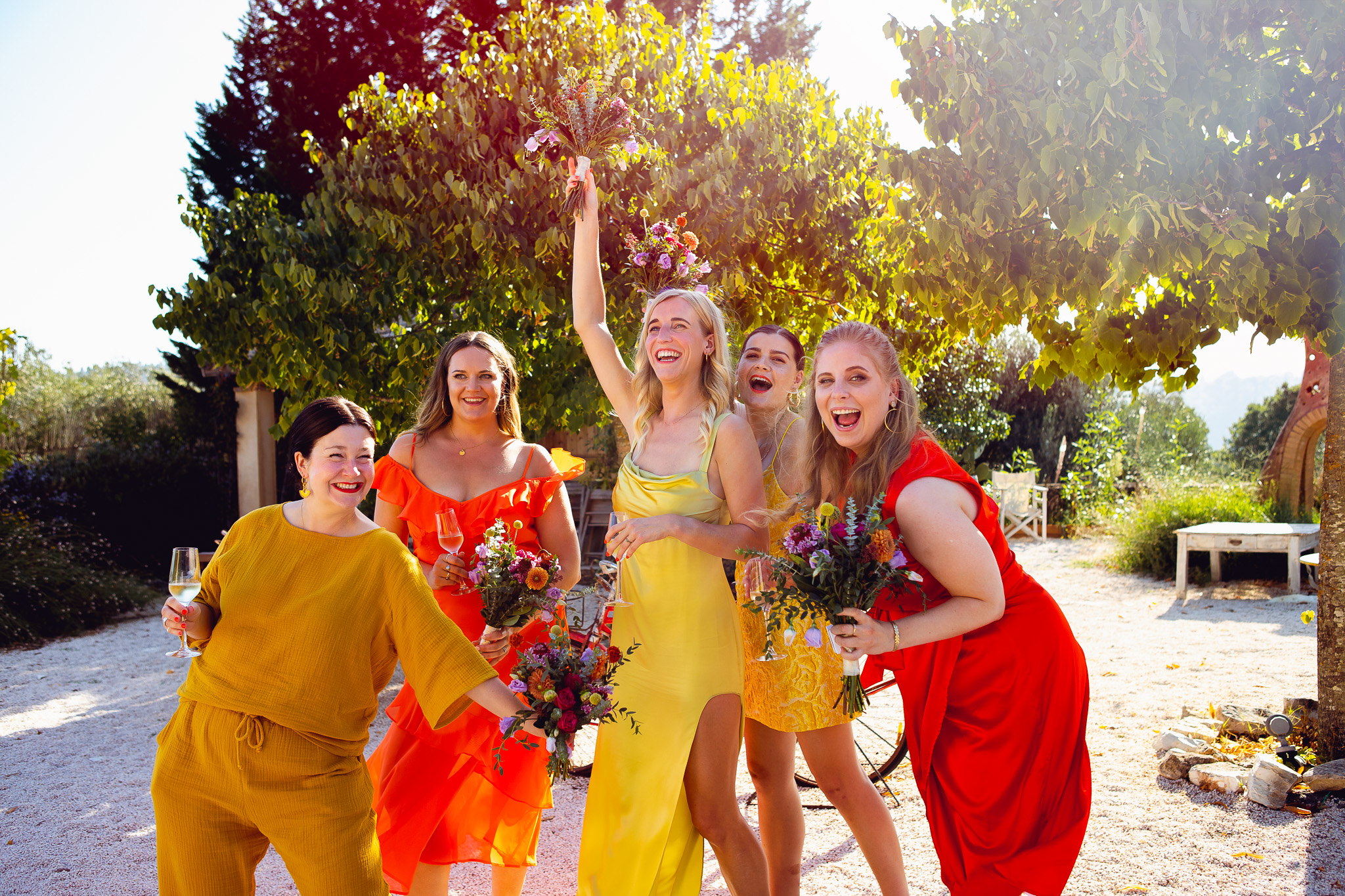 Five brightly dressed bridesmaids laugh and joke around whilst posing at Ambelonas Vineyard, Corfu