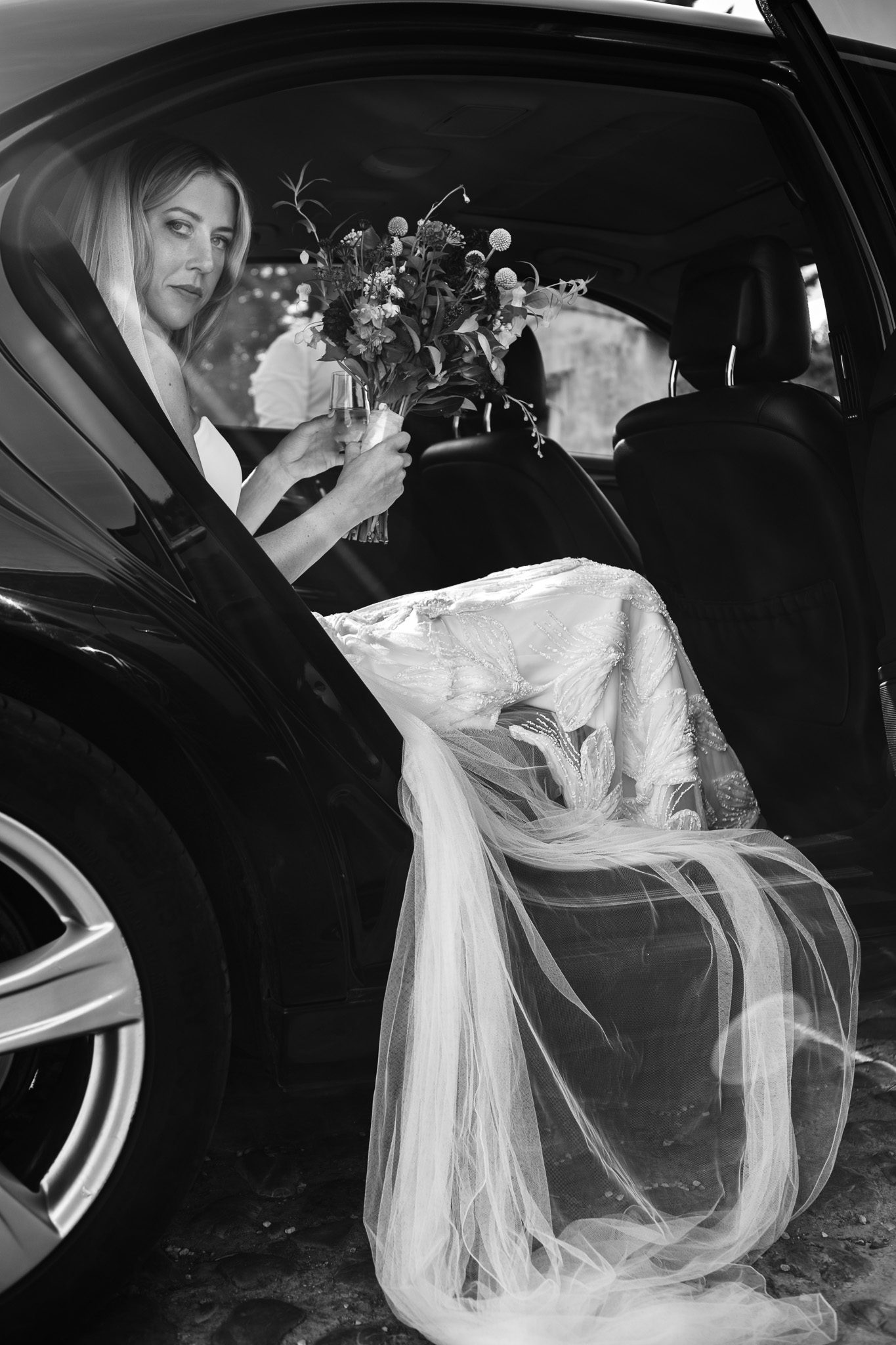 Bride sits in the car and looks out with her dress falling out of the side