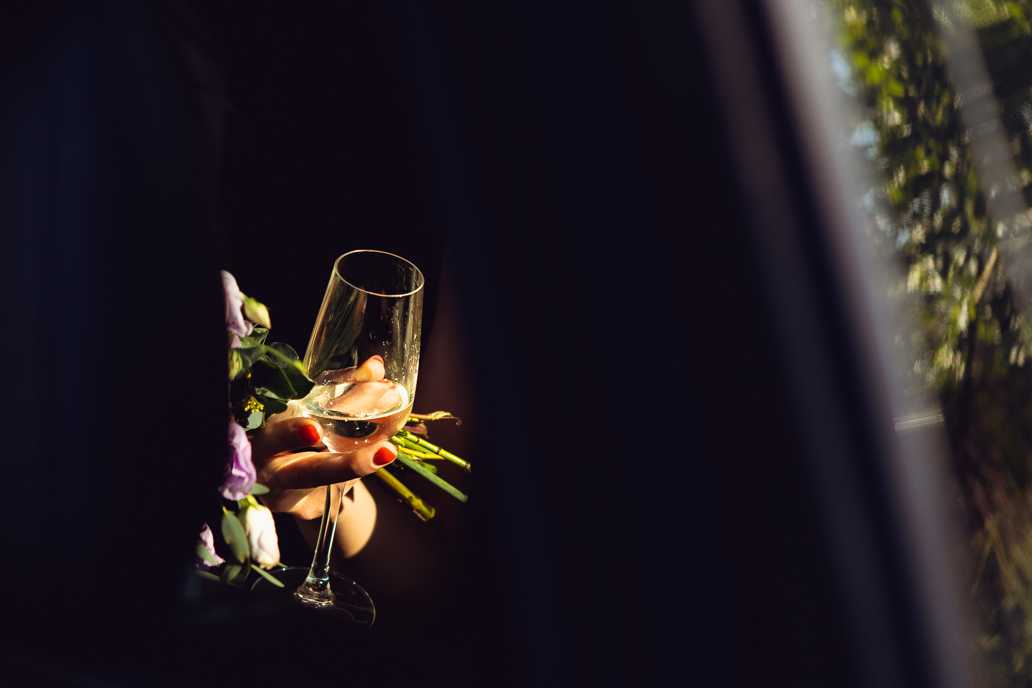 Sun shines on a woman's hand holding a champagne flute and bouquet