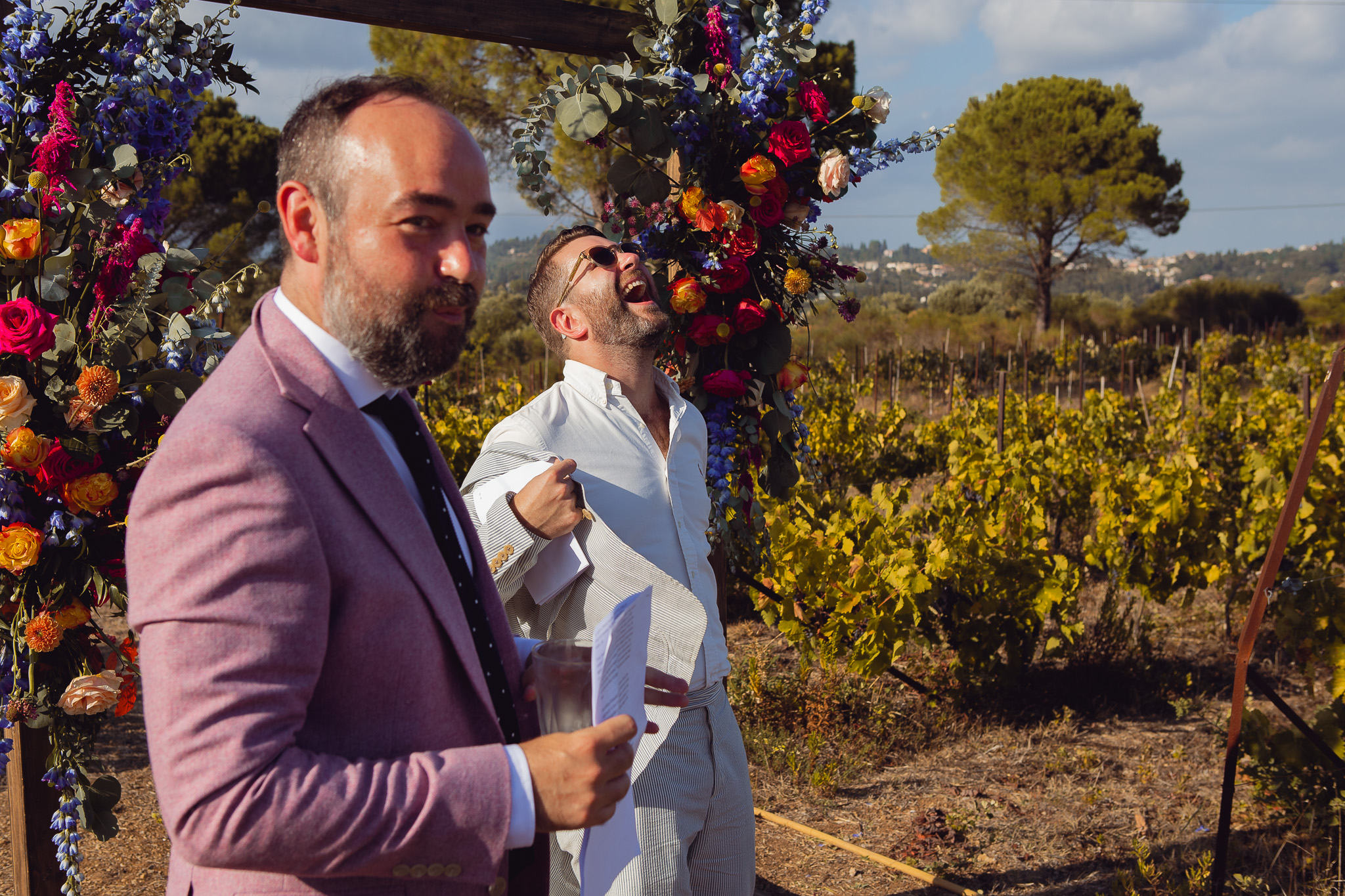 The groom stands at the front of the wedding ceremony waiting for the bride whilst the celebrant laughs