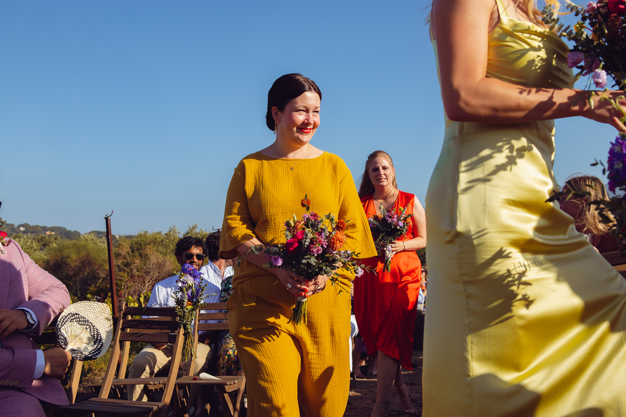 Bridesmaid dressed in yellow walks down the aisle at the wedding ceremony in Ambelonas Vineyard, Corfu