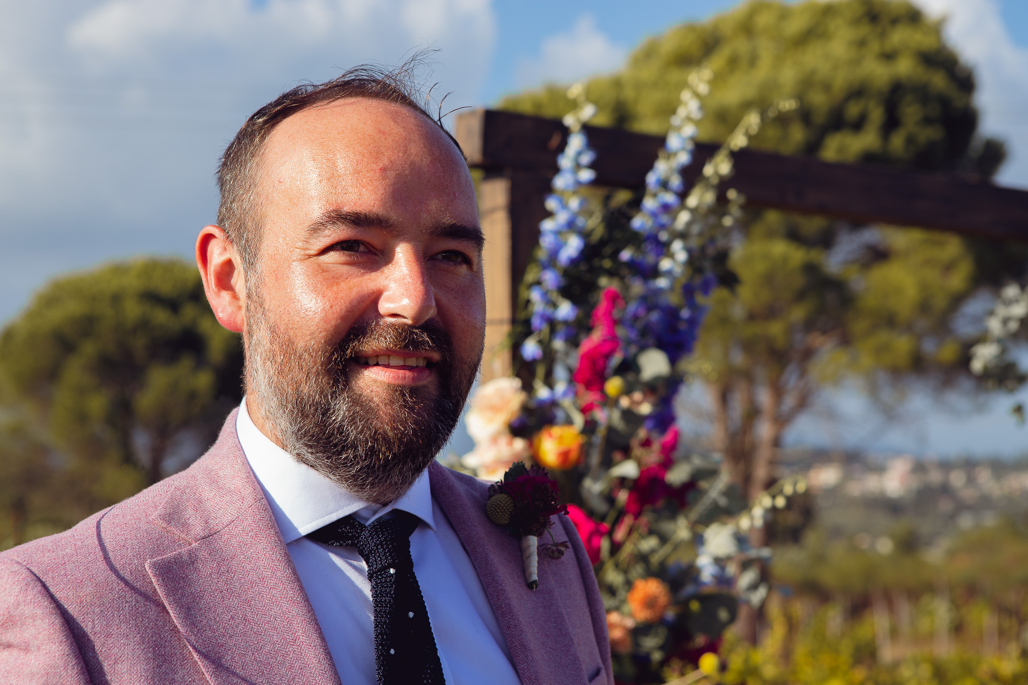 Groom smiles and looks down the aisle to where the bride will be walking at Ambelonas Vineyard, Corfu