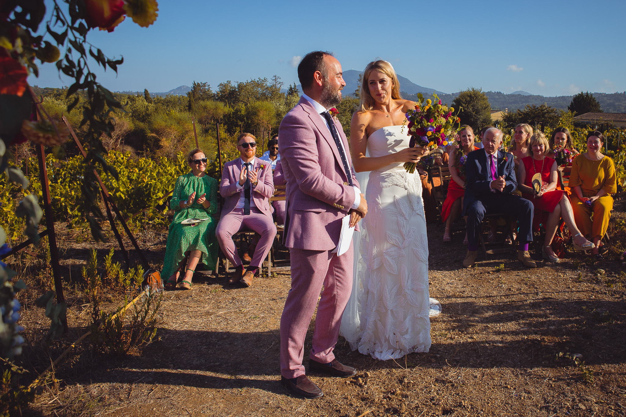 The bride and groom look and smile at each other at their sunny wedding reception in Ambelonas Vineyard, Corfu